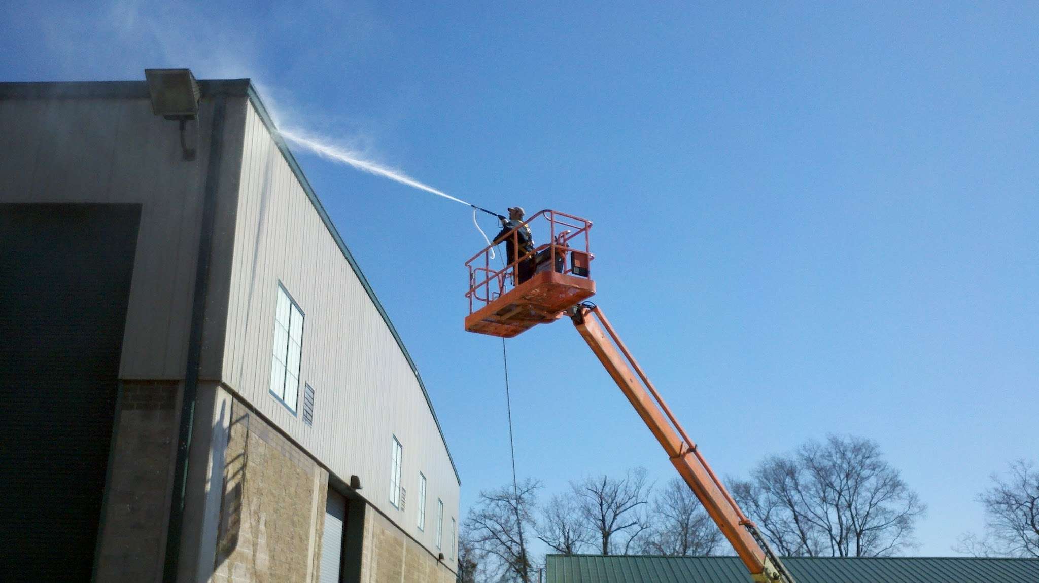 A man in an orange crane spraying water from the side of a building.