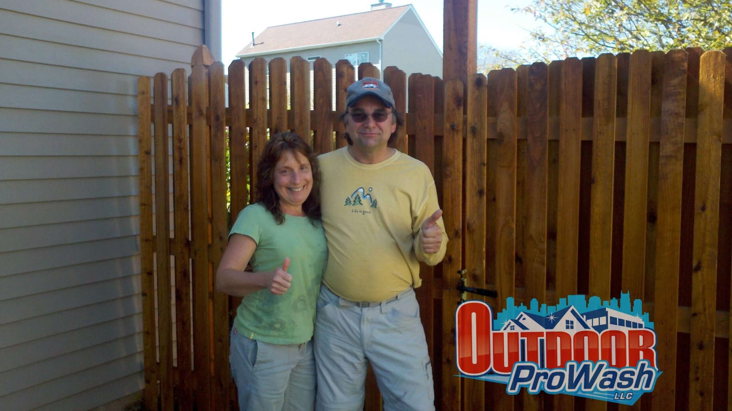 A man and woman posing for the camera in front of a fence.